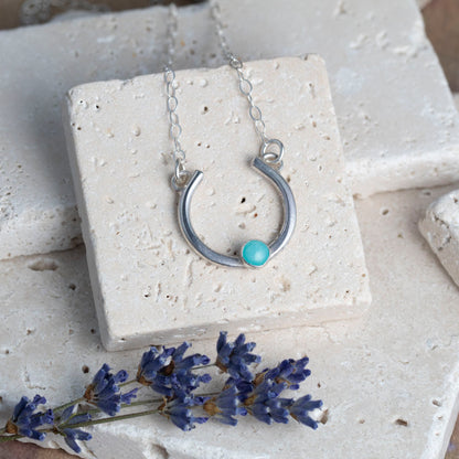 Silver necklace with a amazonite stone on a white stone surface with lavender flowers.