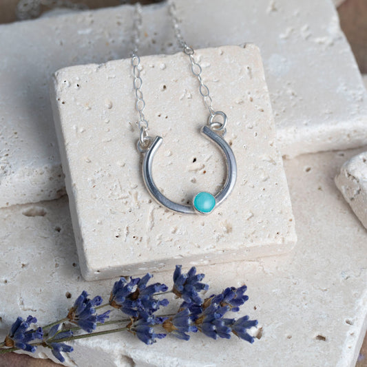 Silver necklace with a amazonite stone on a white stone surface with lavender flowers.