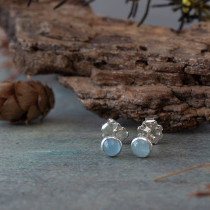 Aquamarine stud earrings set in sterling silver, displayed on a stone surface with bark and natural woodland elements