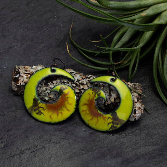 Bright yellow and black spiral enamel earrings with bee motif, handcrafted artisan jewelry inspired by nature and pollinators – unique wearable art by Divella Designs."