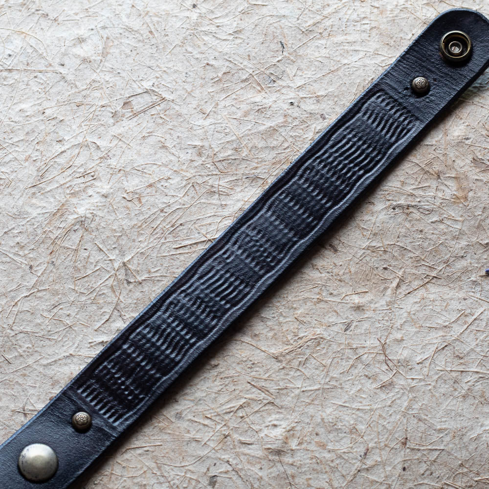 Black leather bracelet with metal buckles on a textured beige background