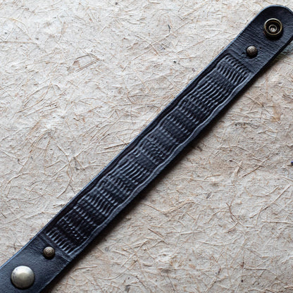 Black leather bracelet with metal buckles on a textured beige background