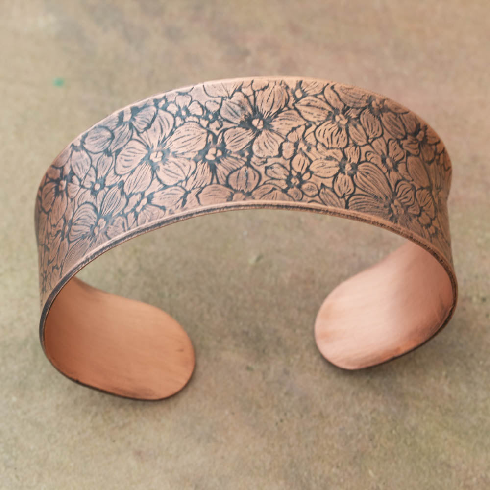Copper bracelet with floral pattern on a textured surface