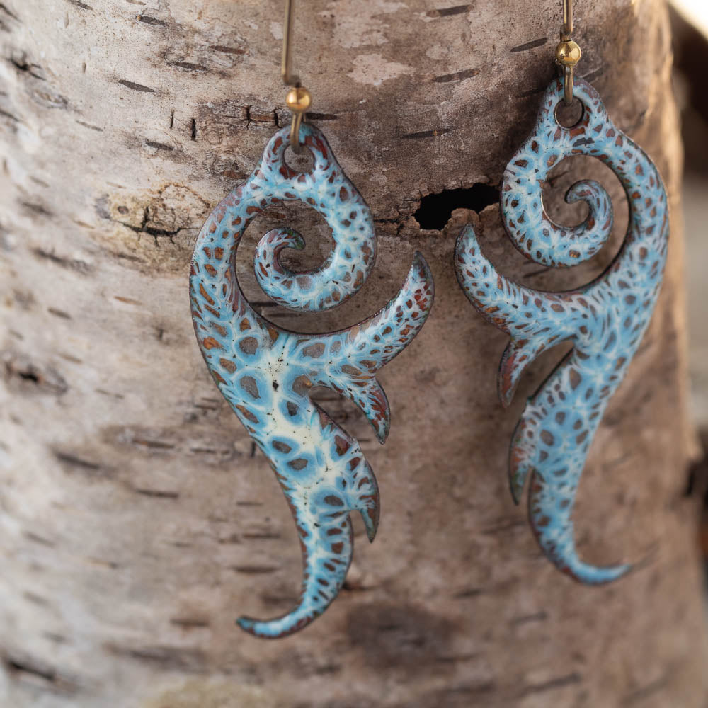 Pair of blue and brown spiral earrings hanging on a wooden surface.