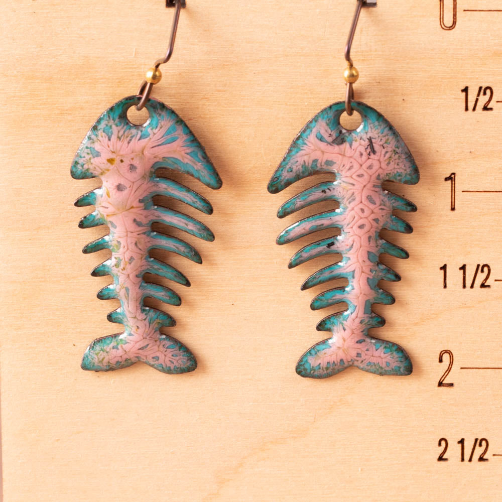 Pair of pink and blue fish bone-shaped earrings on a wooden surface with measurements.