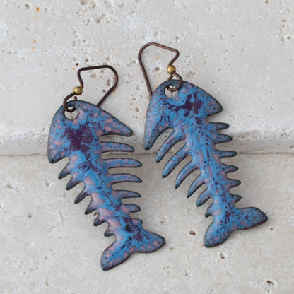 Blue and purple fish skeleton earrings on a light gray background