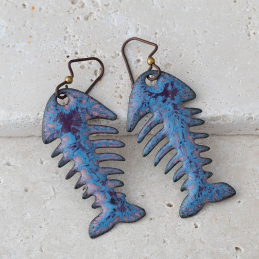 Blue and purple fish skeleton earrings on a light gray background