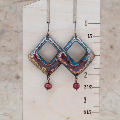 Burgundy, ochre, and teal enamel openwork earrings shown for scale with airy center openings and pearl drops.