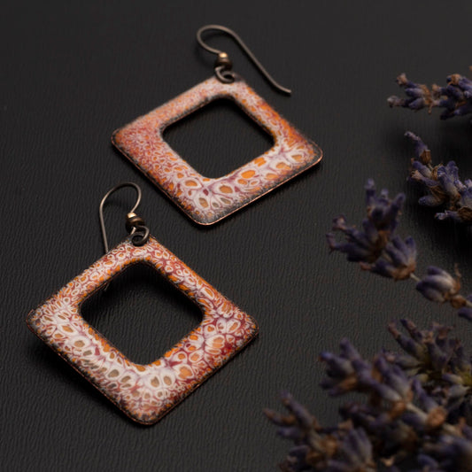 quare copper enamel earrings in earthy orange, rust, and white tones with an organic crackle pattern, displayed on a dark background with sprigs of dried lavender.