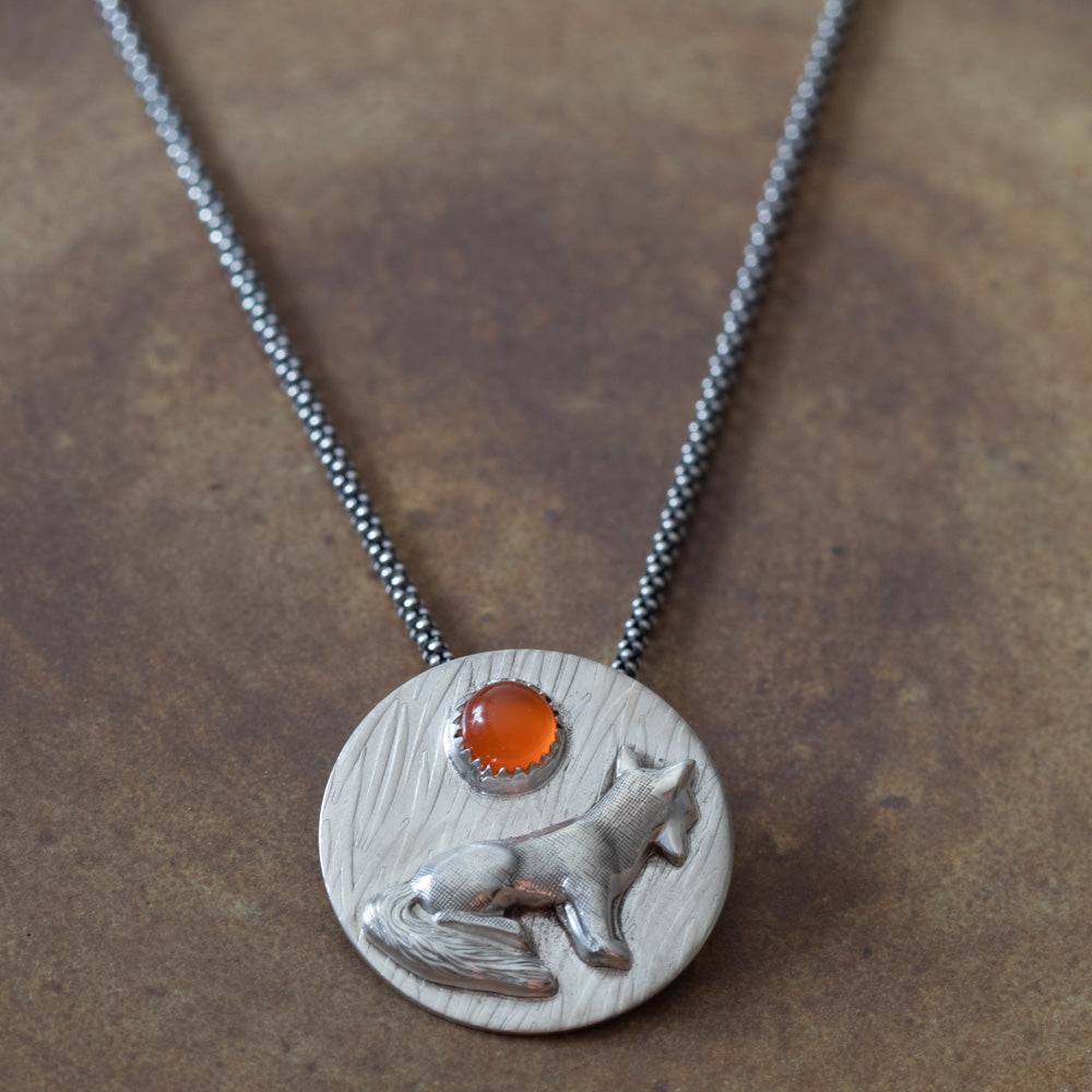 Sterling silver fox pendant necklace with 6mm carnelian on a warm brown background.