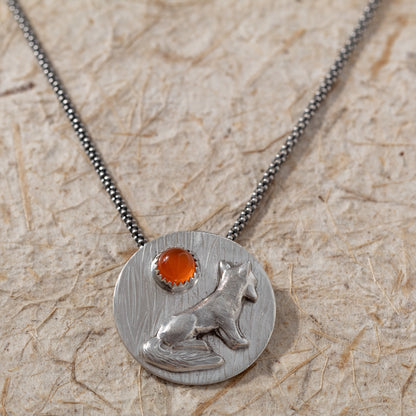 Handmade silver fox pendant with orange carnelian displayed on a light textured background
