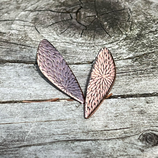 Handcrafted copper post earrings with etched botanical texture – leaf-shaped design, nature-inspired jewelry photographed on rustic weathered wood background.
