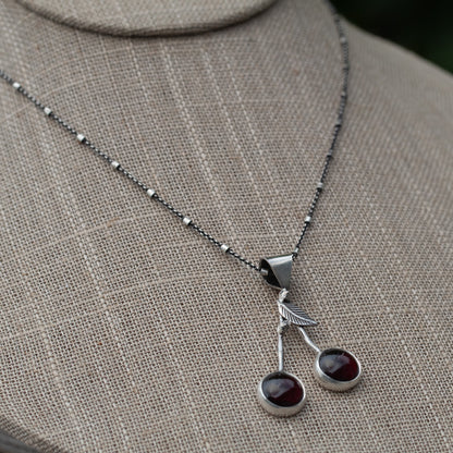 Garnet cherry sterling silver necklace shown on a display form to demonstrate its 1 1/2-inch pendant drop and 18-inch chain.