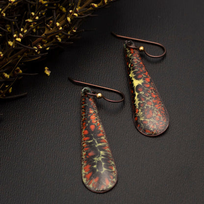Dark orange and black enamel teardrop earrings with yellow veining, displayed on a gray slate with autumn florals.