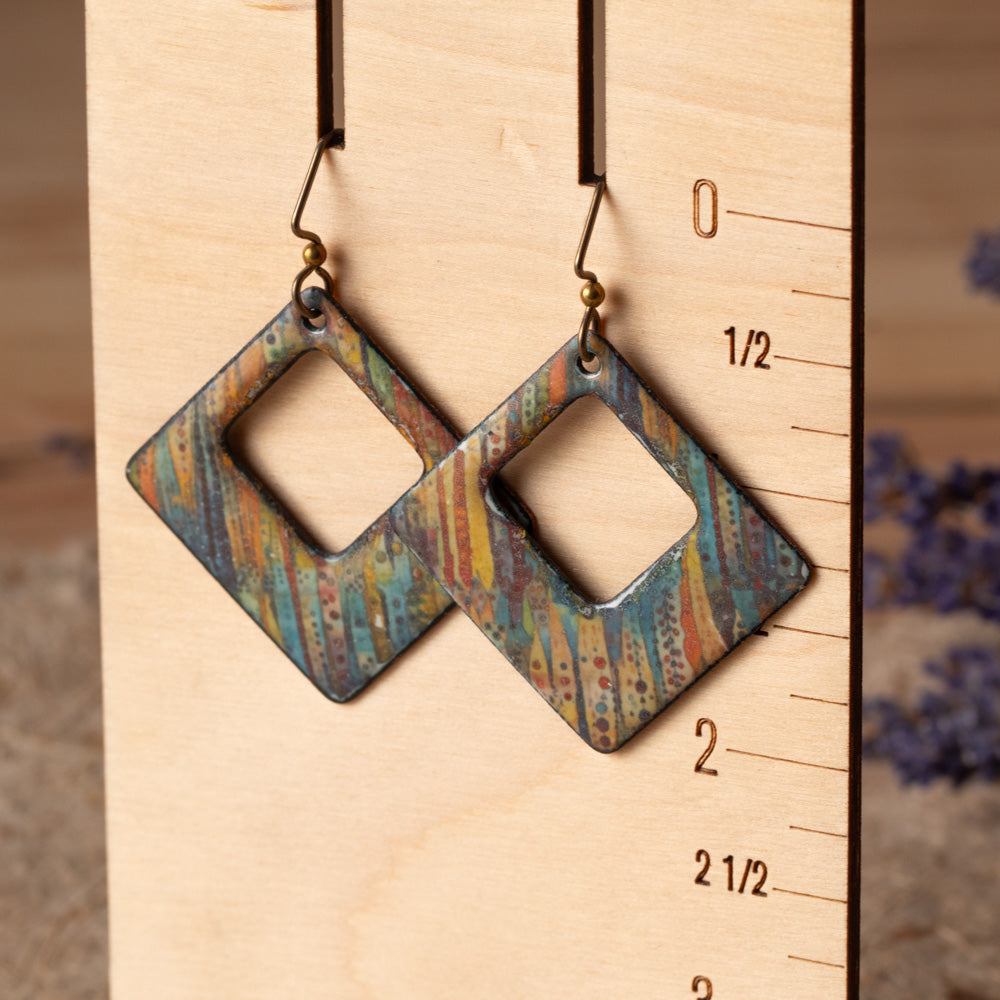 Colorful open square enamel earrings with teal, gold, rust, and orange line details on niobium ear wires.