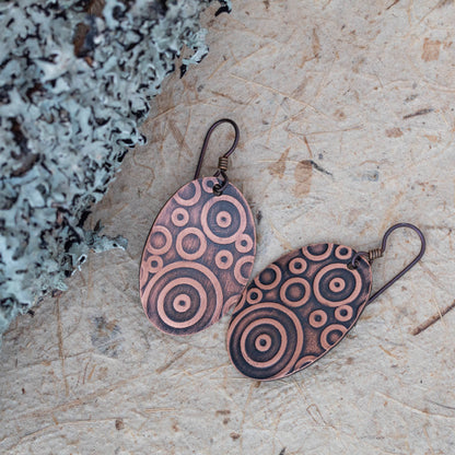 Handmade copper dangle earrings with etched concentric circle pattern, featuring an oval shape, oxidized finish, and modern rustic artisan style