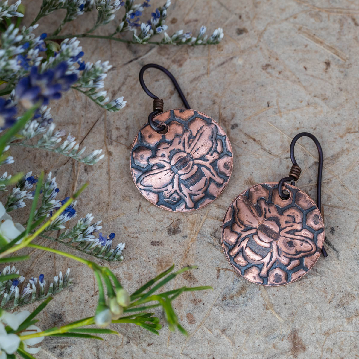 Handcrafted copper bee and honeycomb earrings with etched texture, featuring round disc shape and oxidized finish for rustic, nature-inspired artisan jewelry