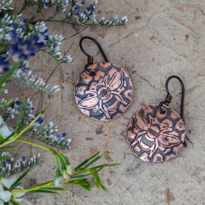 Handcrafted copper bee and honeycomb earrings with etched texture, featuring round disc shape and oxidized finish for rustic, nature-inspired artisan jewelry
