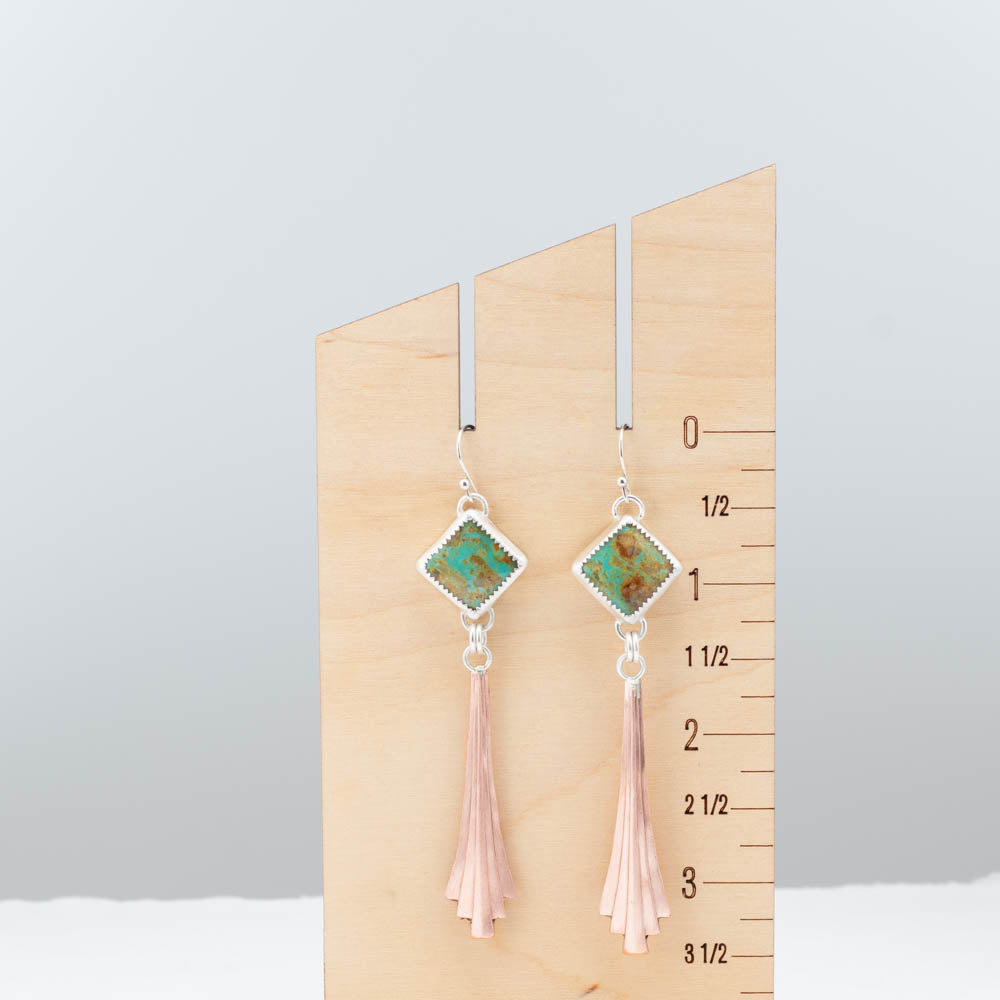Pair of earrings with square gemstones and copper tassels on a wooden ruler for scale.