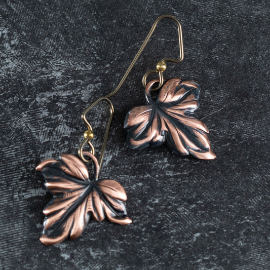 handmade copper maple leaf earrings with dark patina and niobium ear wires on textured dark background