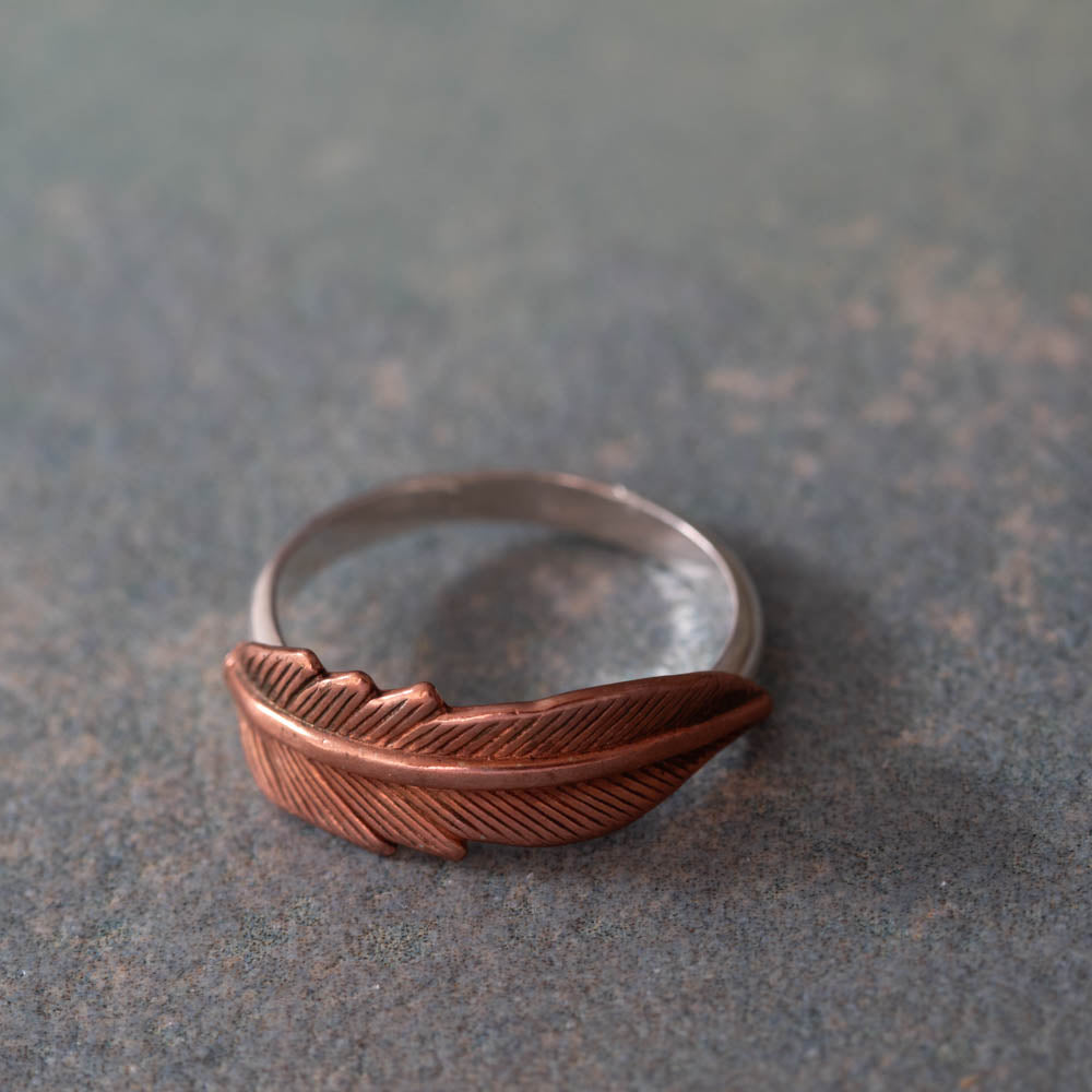 Copper feather ring on sterling silver band with detailed texture on a neutral background