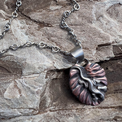 Handcrafted sterling silver and copper pendant necklace featuring a sculpted lizard on a textured leaf background, with oxidized finish and nature-inspired artisan design. Hanging on a handmade sterling chain