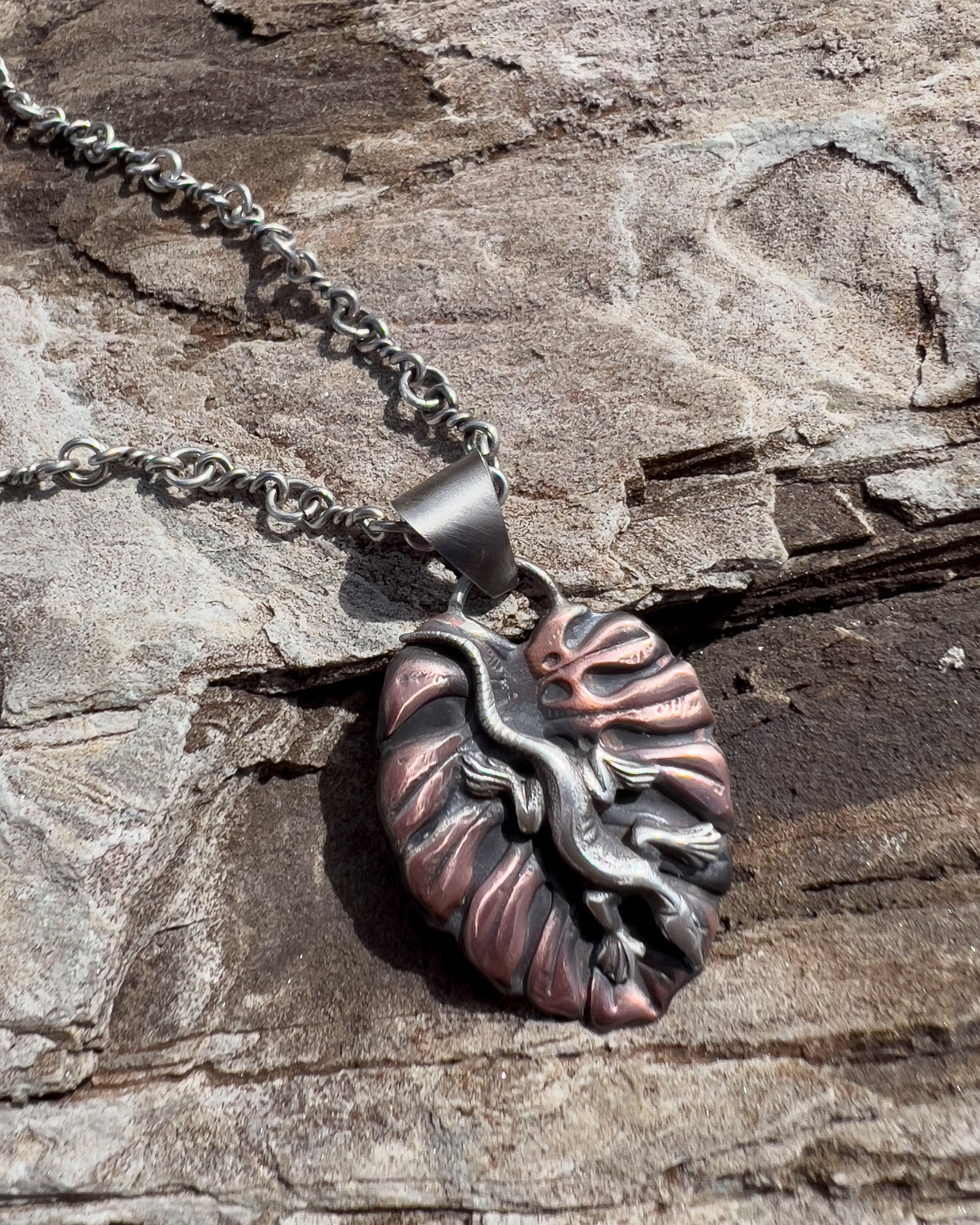 Handcrafted sterling silver and copper pendant necklace featuring a sculpted lizard on a textured leaf background, with oxidized finish and nature-inspired artisan design.