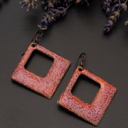 Square-shaped cranberry red enamel earrings with a delicate crackle pattern, displayed on a black background beside sprigs of lavender.