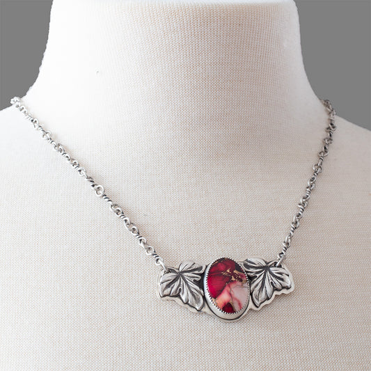 Crimson Bloom necklace with oval dahlia rose stone in pink and red, framed by two detailed sterling silver leaves on a handcrafted silver chain, botanical artisan jewelry.