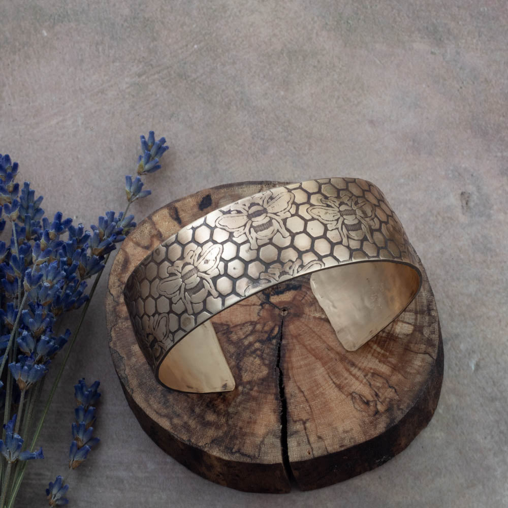 Brass bracelet with intricate patterns on a textured surface with lavender flowers.