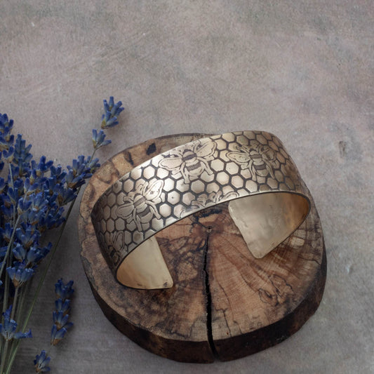 Brass bracelet with intricate patterns on a textured surface with lavender flowers.