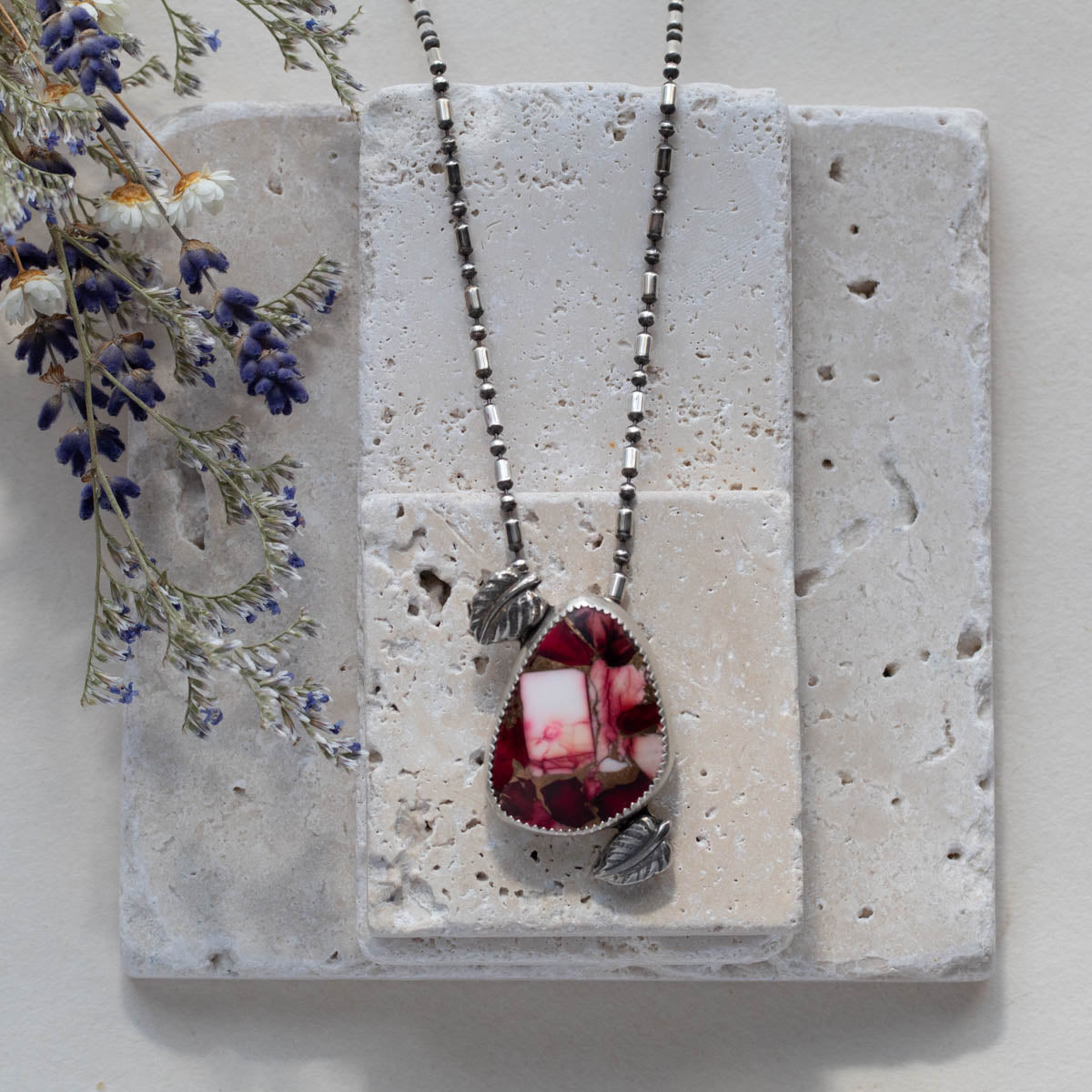 Handmade sterling silver pendant necklace featuring a red and pink dahlia jasper stone with leaf accents, set on a beaded oxidized chain for a nature-inspired artisan look.