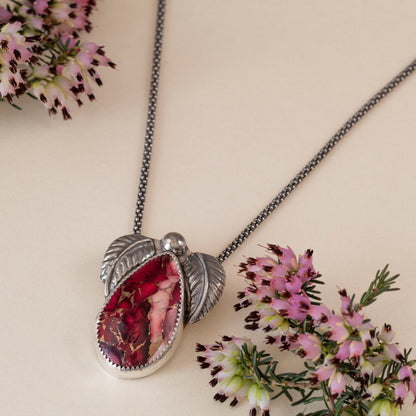 Sterling silver necklace with teardrop dahlia jasper stone in shades of pink and red, accented by two detailed silver leaves and a polished silver bead, handmade botanical jewelry.