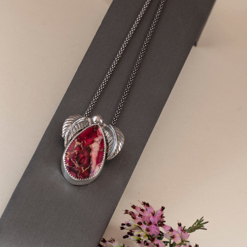 Sterling silver necklace with teardrop dahlia jasper stone in shades of pink and red, accented by two detailed silver leaves and a polished silver bead, handmade botanical jewelry.