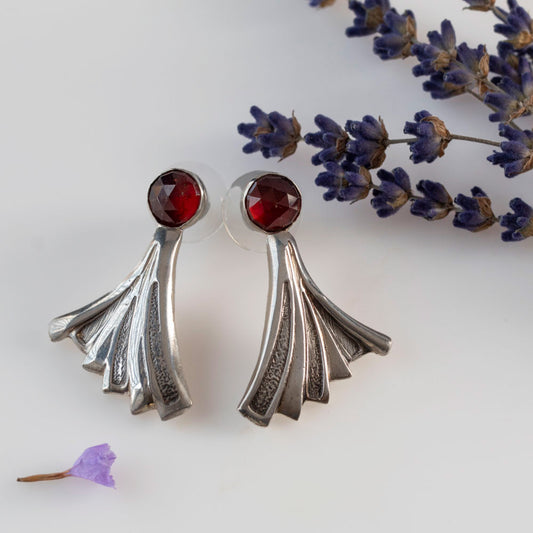 Art Deco-inspired sterling silver earrings featuring deep red faceted garnet stones and flared geometric fan shapes, styled with dried lavender for a vintage botanical vibe