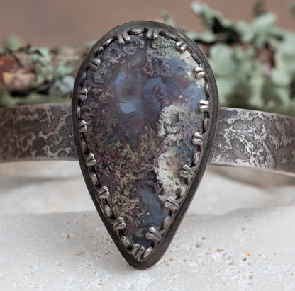 Dendritic moss agate sterling silver cuff bracelet with large teardrop stone, lichen-like pattern, textured silver cuff, and oxidized handmade finish by Divella Designs.