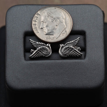 Silver winged earrings on a black display block with a dime for scale.