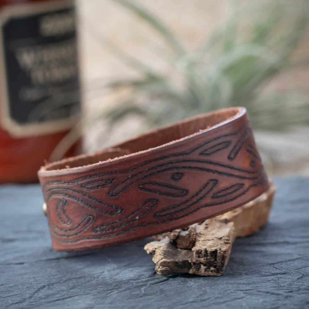 Brown leather bracelet with embossed design on a textured surface with a blurred background