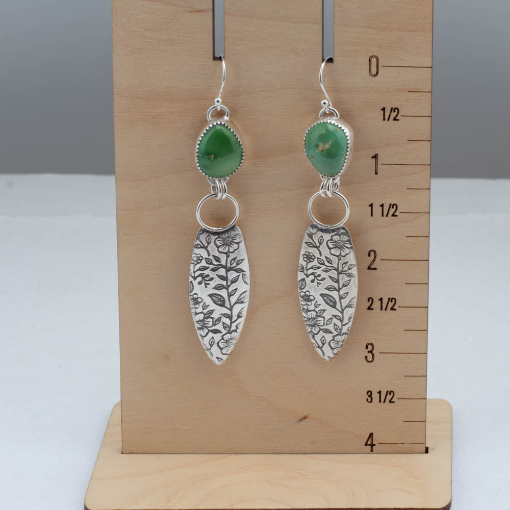 Silver earrings with emerald valley turquoise stones on a wooden stand with measurement