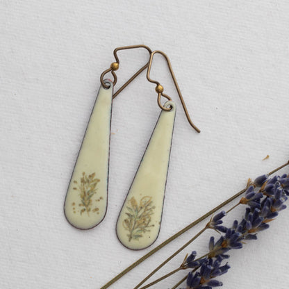 Teardrop-shaped  enamel earrings with floral details on a white background with lavender.