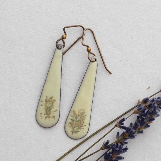 Teardrop-shaped  enamel earrings with floral details on a white background with lavender.