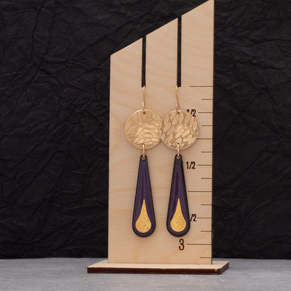 Purple enamel teardrop earrings featuring 24k gold droplet accents and round hammered brass discs, displayed on a wooden ruler for scale.