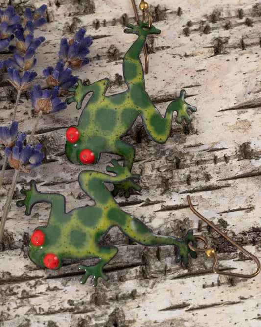 Playful green frog-shaped enamel earrings with bright red eyes, handcrafted and displayed on birch bark with dried lavender – Enchanted Frog design by Divella Design