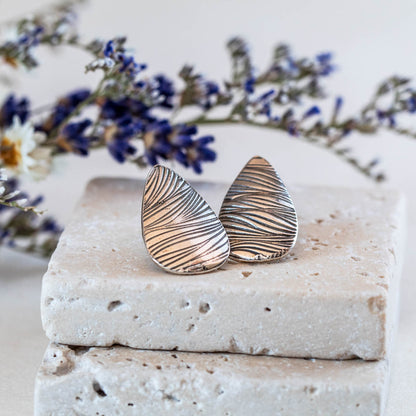 Handmade sterling silver teardrop stud earrings with etched line texture, featuring a minimalist nature-inspired design and oxidized finish.