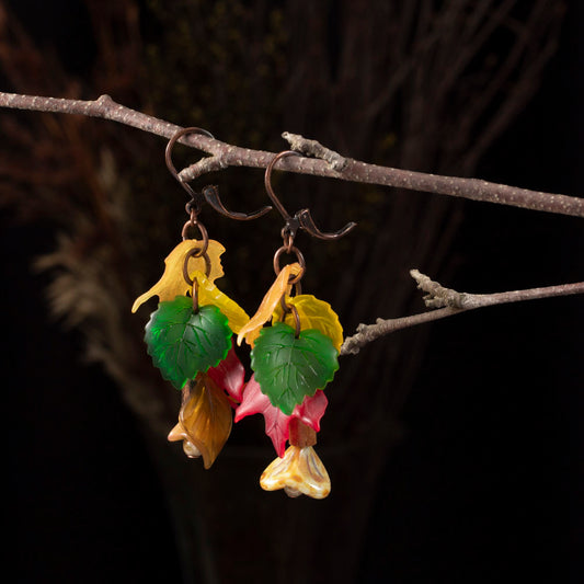 Colorful lucite leaf earrings in red, green, and yellow hanging from a twig, with copper ear wires and floral details, fall-themed handmade jewelry.