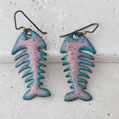 Pair of fish-shaped earrings with pink and blue design on a textured white background