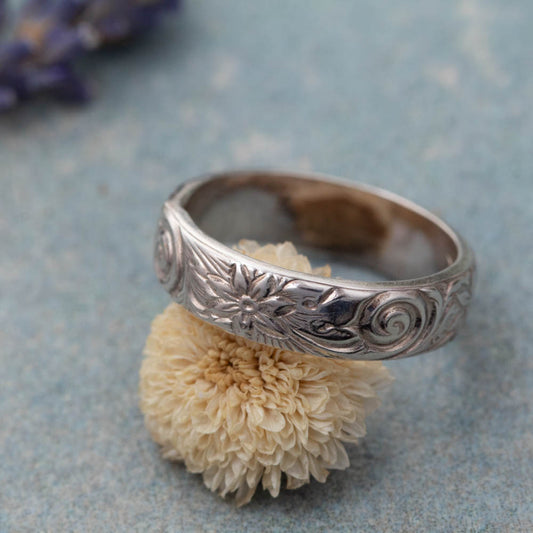Handmade silver ring with detailed floral pattern resting on dried flower