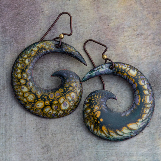 Handcrafted spiral enamel earrings in deep forest green with golden ember and violet highlights, featuring a lichen-like texture and niobium ear wires, displayed on a textured background.