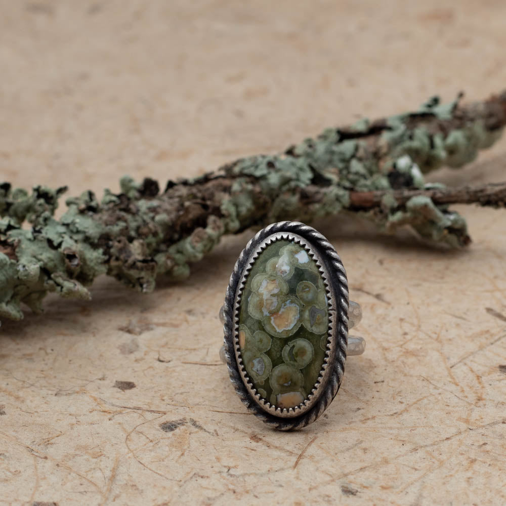 Rainforest Jasper ring on bark with lichen covered branch in the background