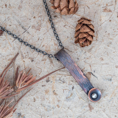 Hand-forged copper pendant necklace with rustic texture and silver accent, featuring a minimalist vertical bar design on oxidized chain for earthy artisan style.